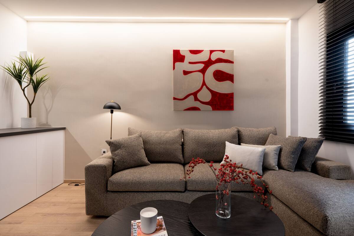 Un salon moderne avec un canapé gris, une table basse noire et un tableau abstrait rouge accroché au mur.
