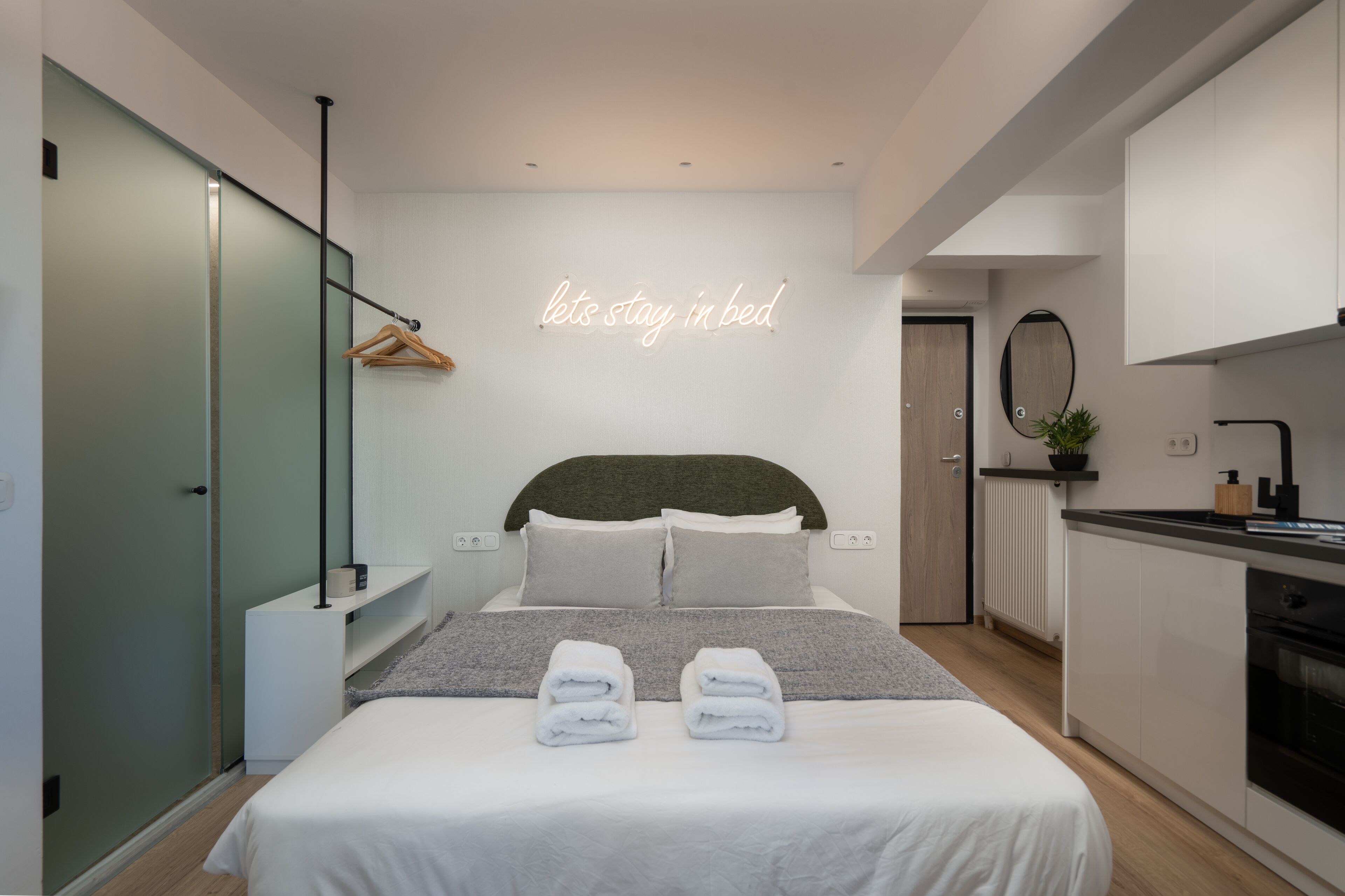 Un dormitorio moderno con cama, mesitas de noche, un perchero para toallas y una cocina, además de una pared decorada con un letrero de neón.