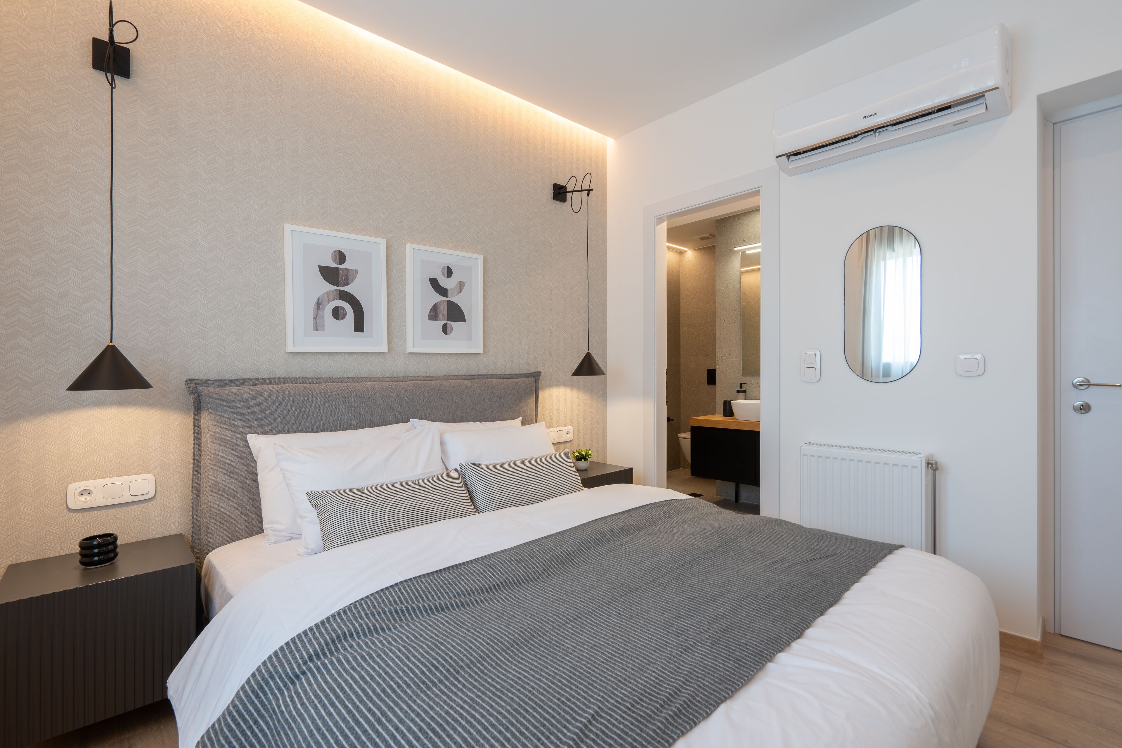 Ein modernes Schlafzimmer mit einem großen Bett, Nachttischlampen, einer Wand-Klimaanlage und gerahmten Kunstwerken.