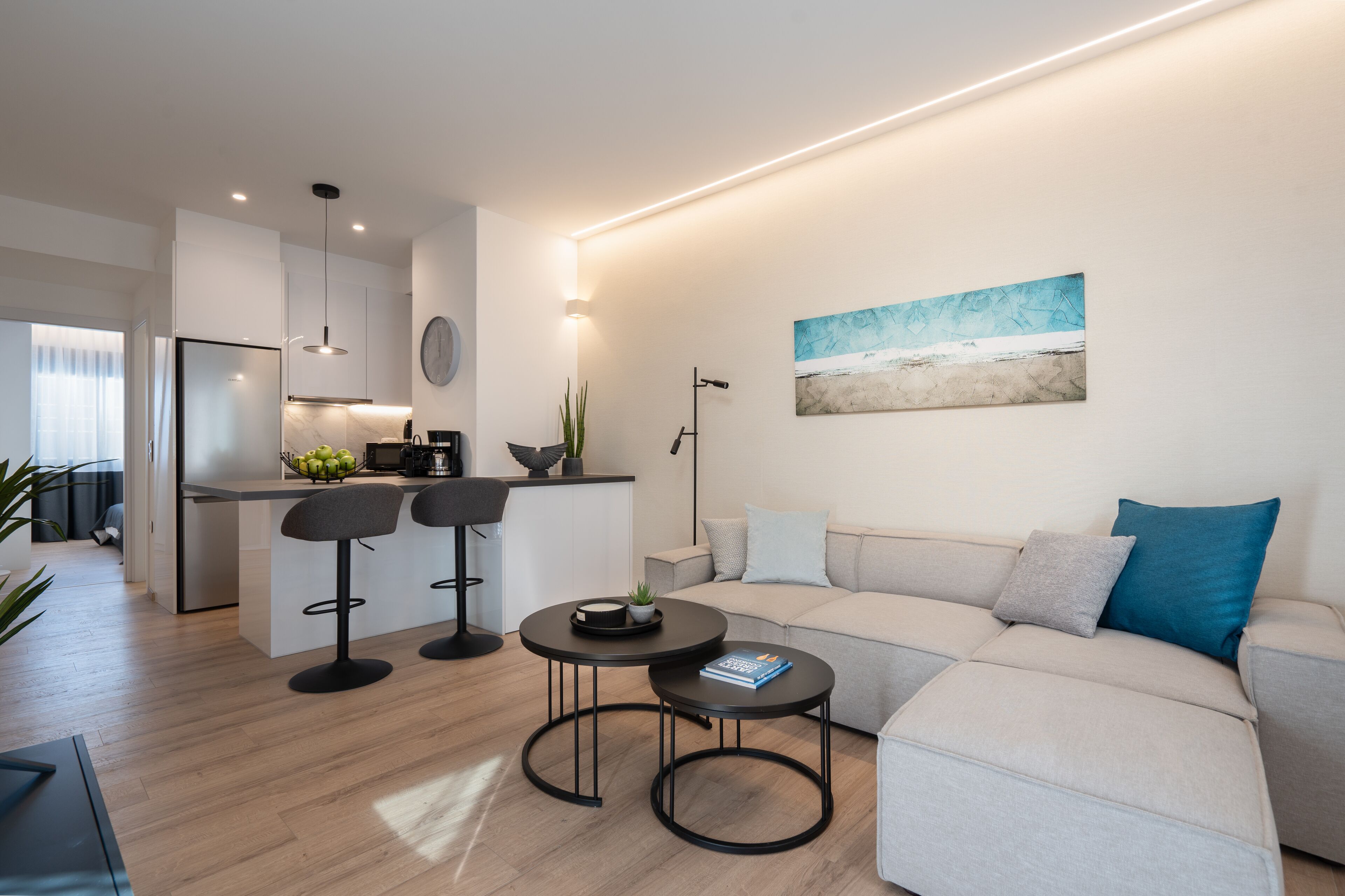 Una sala de estar moderna con un sofá, dos mesas redondas y una cocina al fondo.