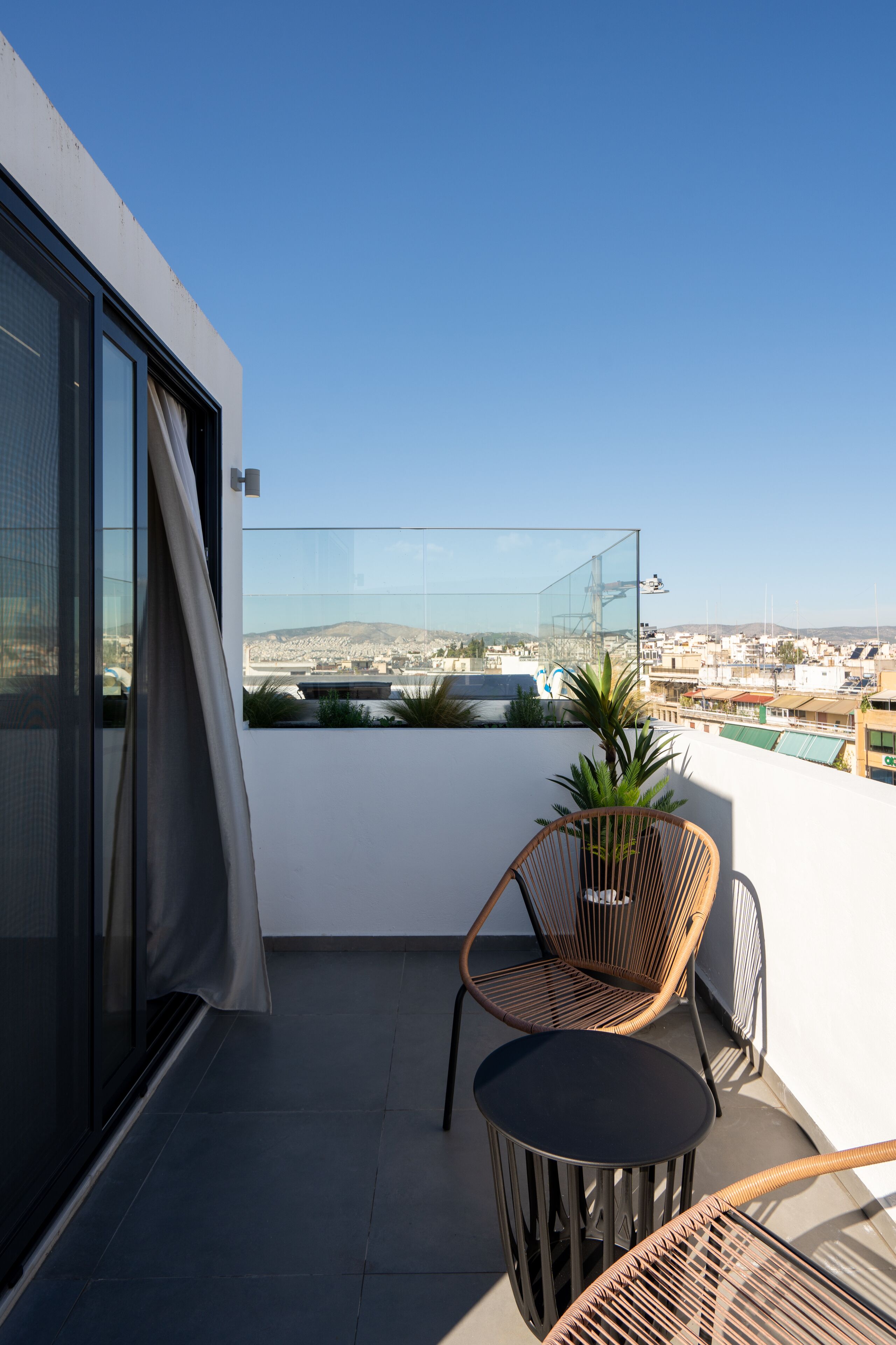 Un balcone con una parete divisoria in vetro, una sedia in vimini, un tavolino e una pianta in vaso.