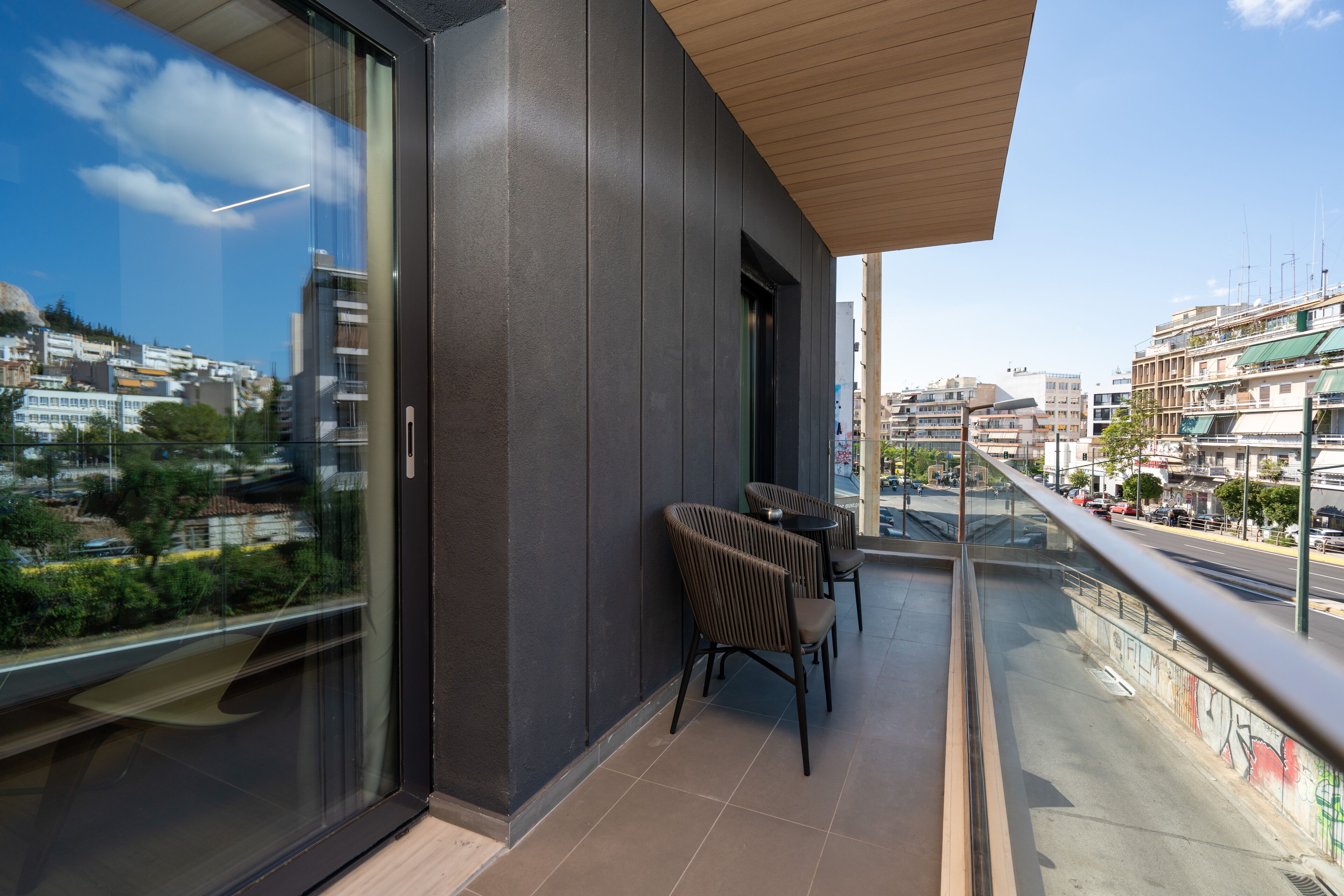 Un balcón moderno con vista a la ciudad, que cuenta con barandilla de vidrio y techo de madera.