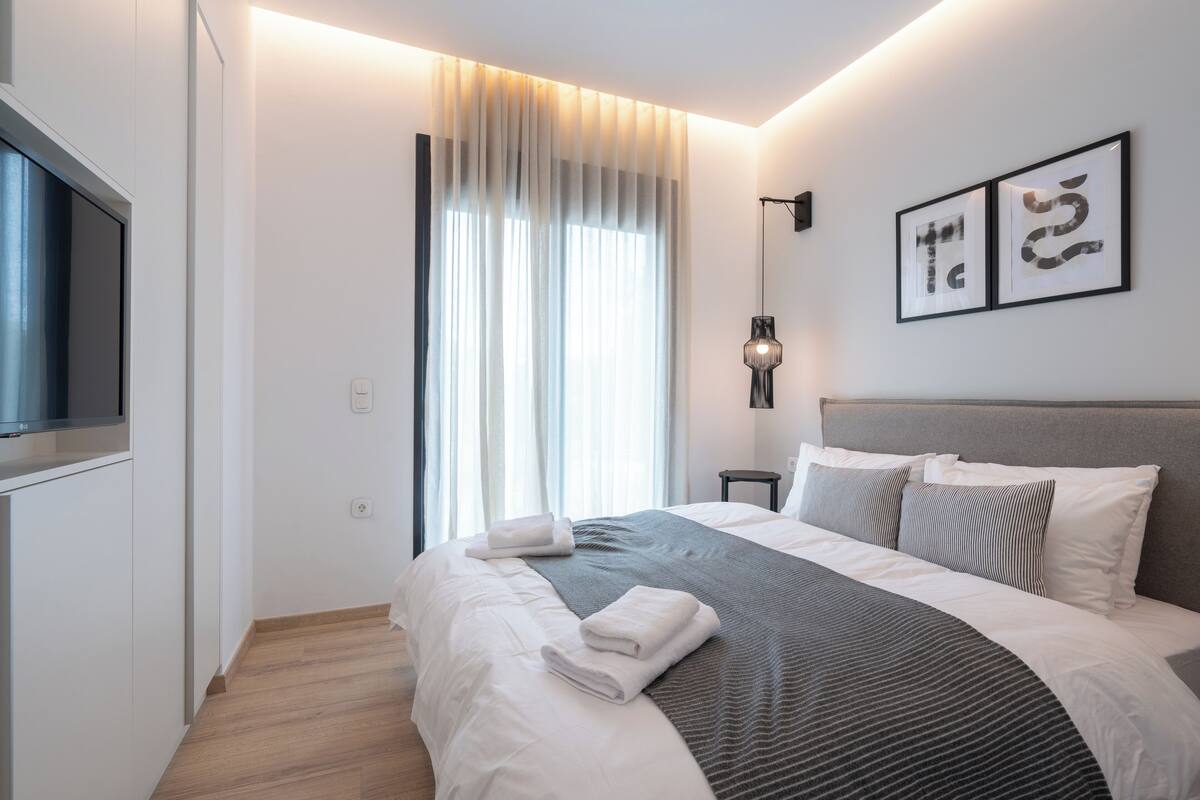 Une chambre d’hôtel moderne avec un grand lit, un téléviseur à écran plat et une fenêtre agrémentée de rideaux légers.