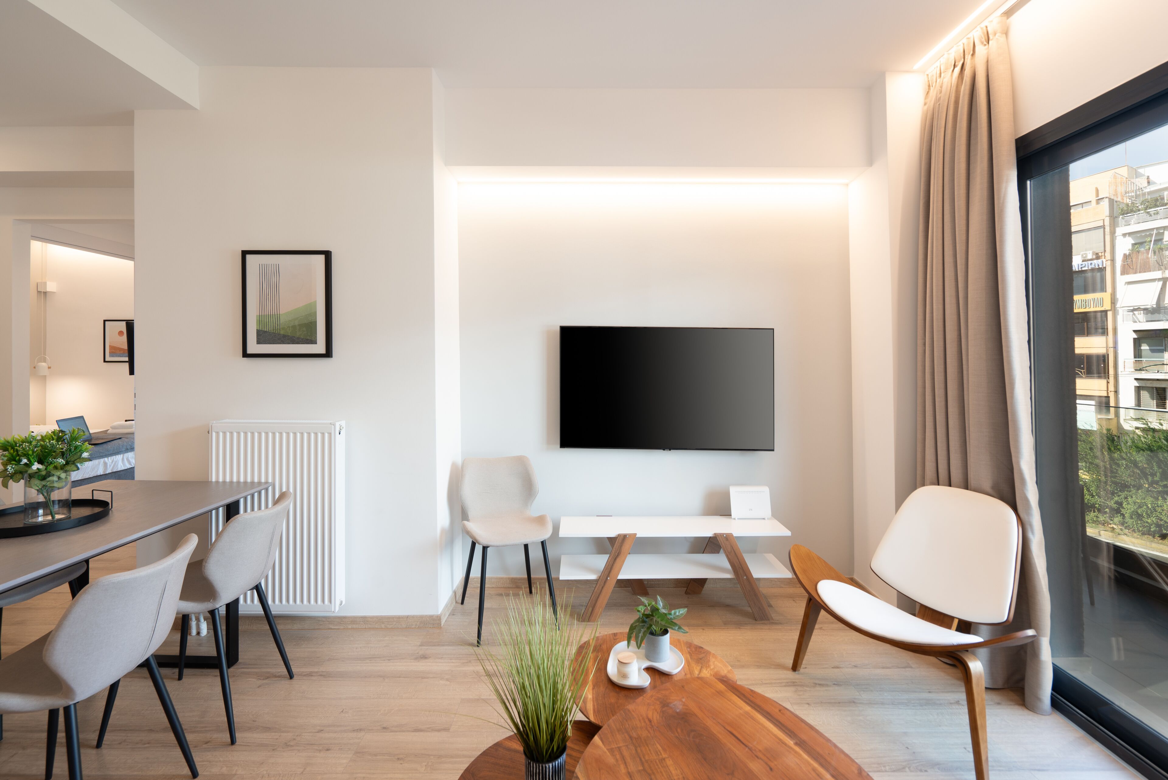Un salon moderne comprenant un coin repas, un téléviseur à écran plat fixé au mur et une grande fenêtre avec des rideaux.