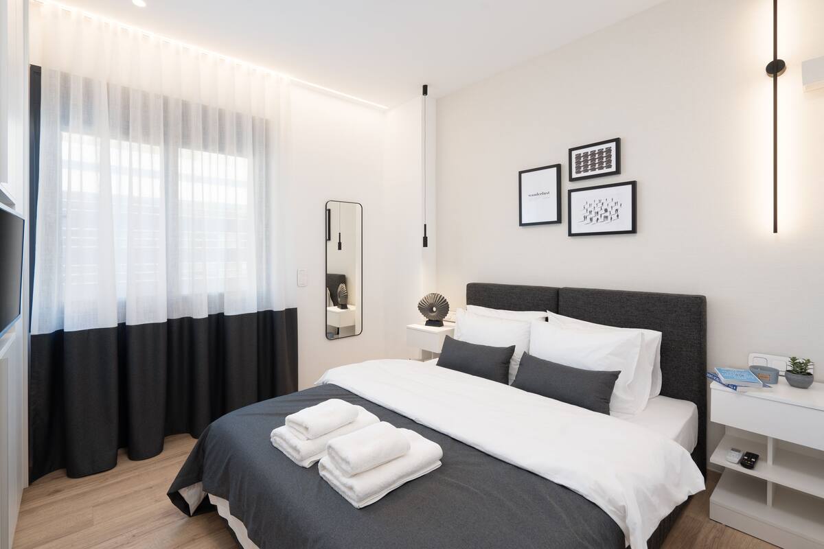 Une chambre d’hôtel moderne avec un grand lit, une table de chevet avec une lampe, un miroir et des œuvres d’art encadrées accrochées au mur.