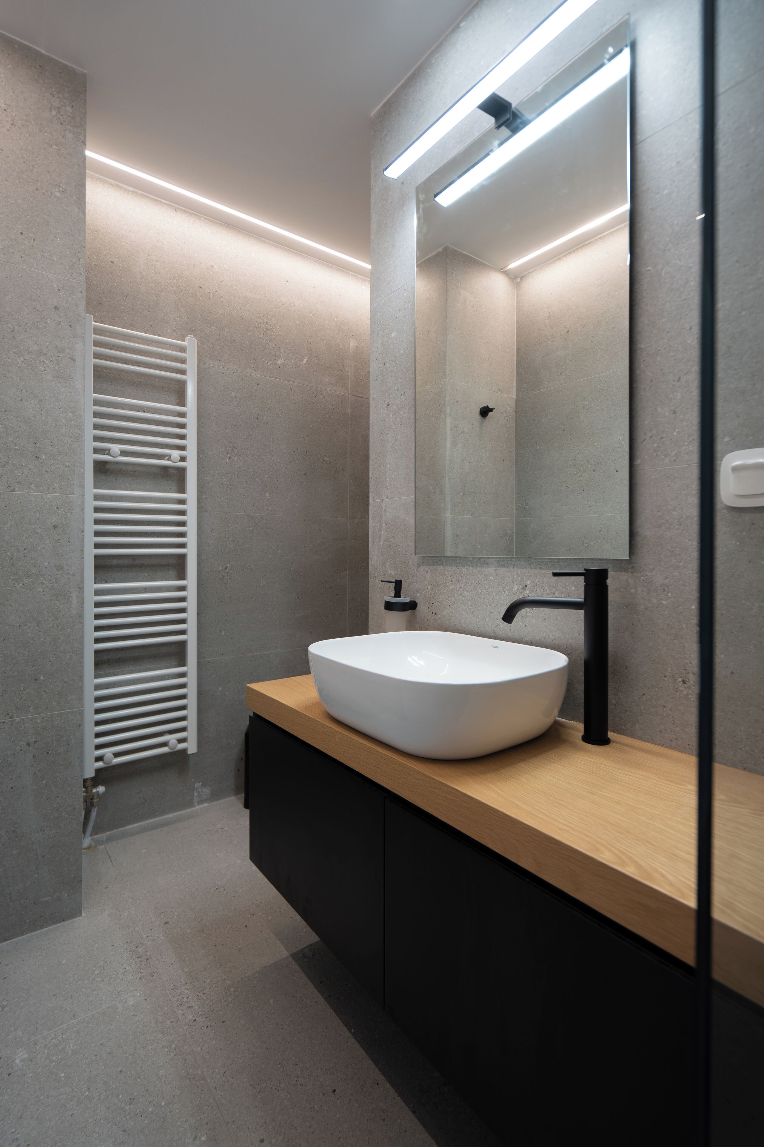 A modern bathroom with a white vessel sink, a wooden vanity, a large mirror, and a towel rack.