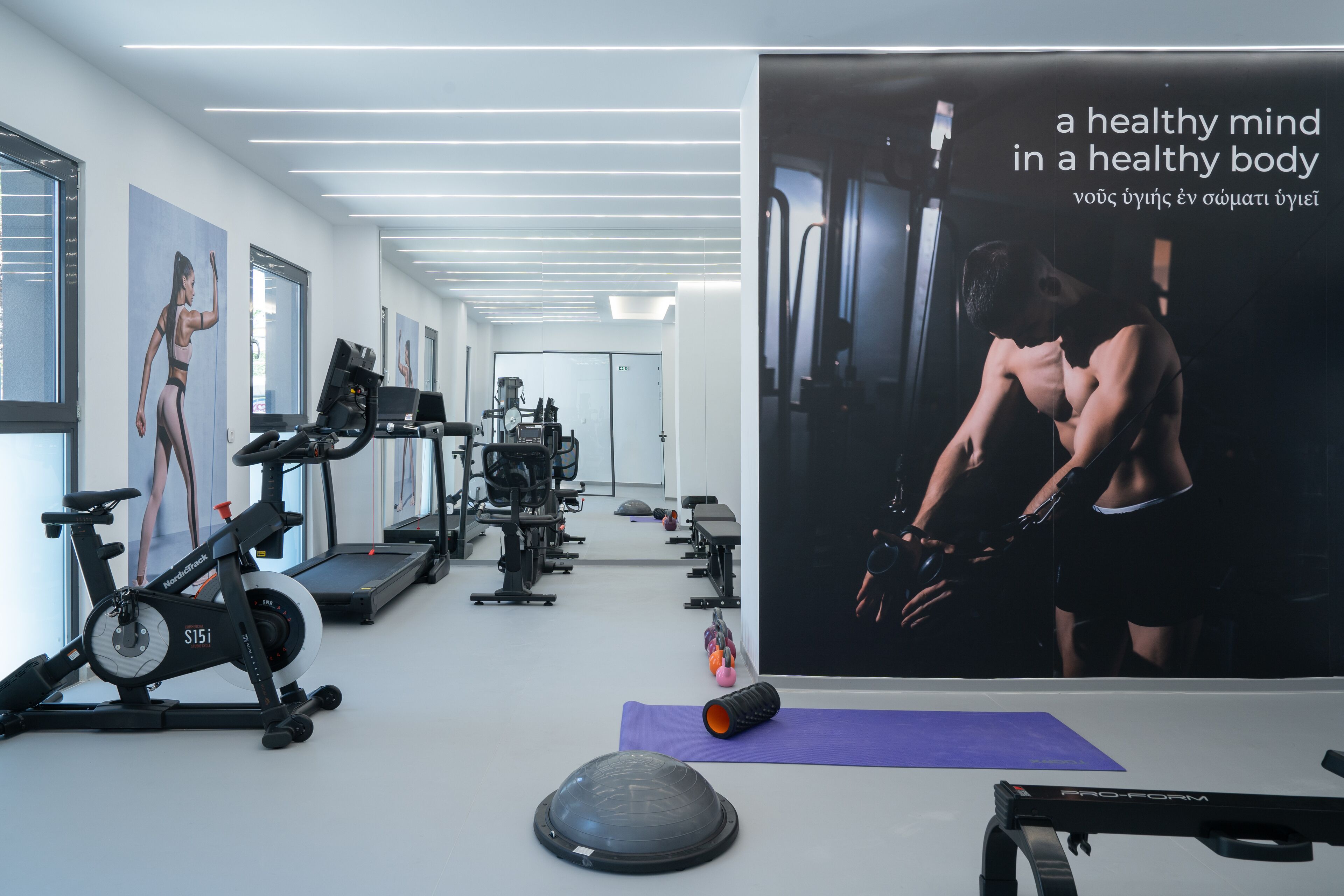 A modern gym with various exercise equipment, including treadmills and stationary bikes, and a motivational poster on the wall.