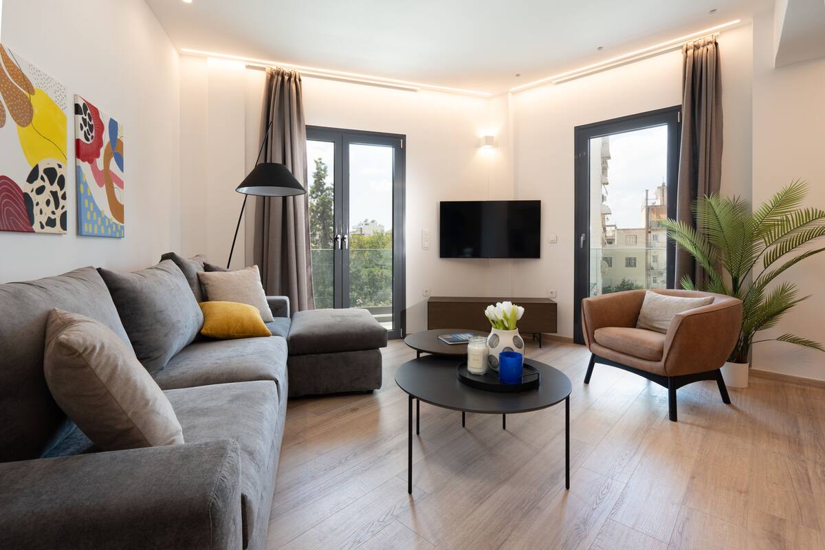 Un salon moderne avec un canapé gris, un fauteuil marron, une table basse, un téléviseur à écran plat et une plante en pot.