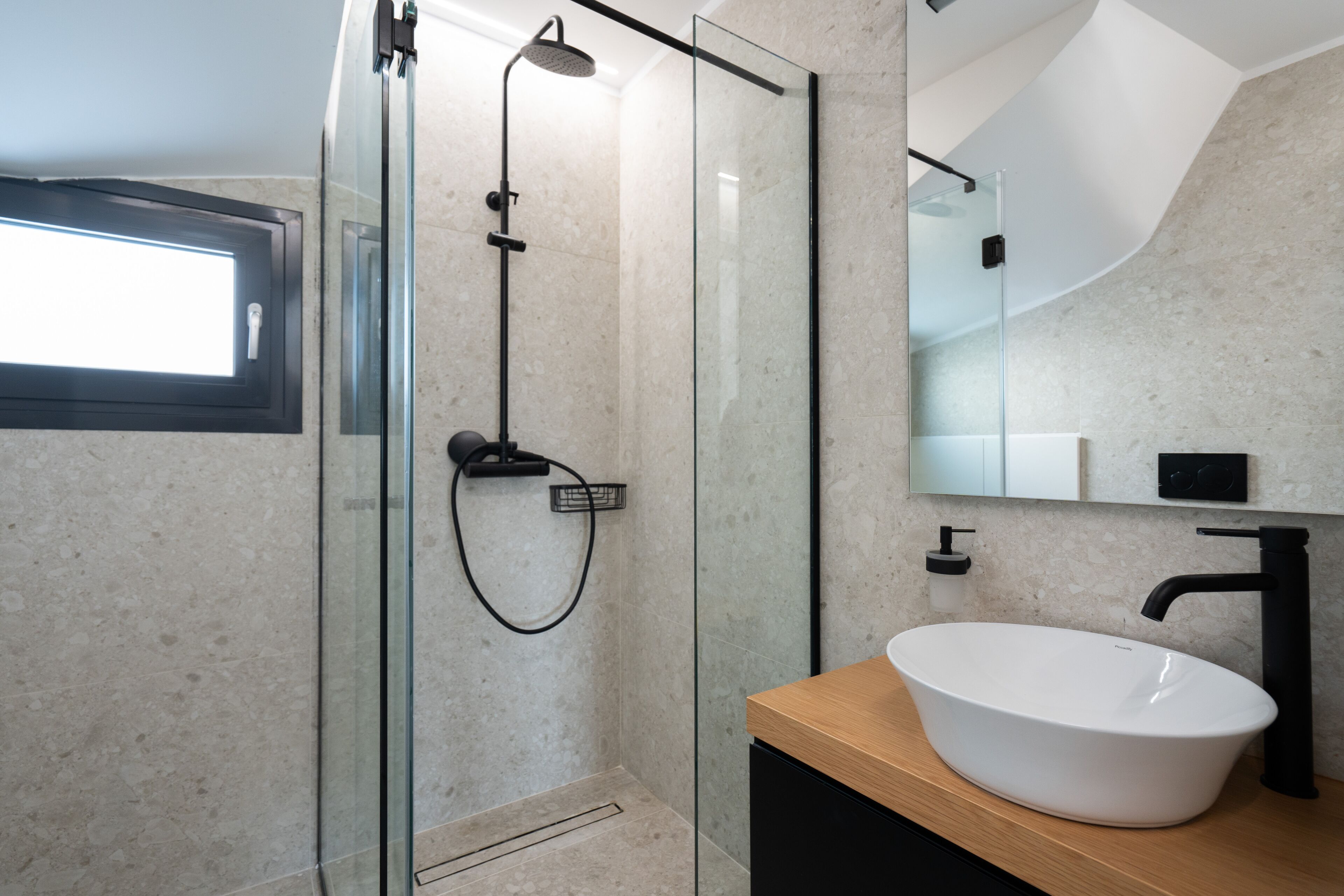 Un baño moderno con cabina de ducha acristalada, un lavamanos blanco y una encimera de madera.