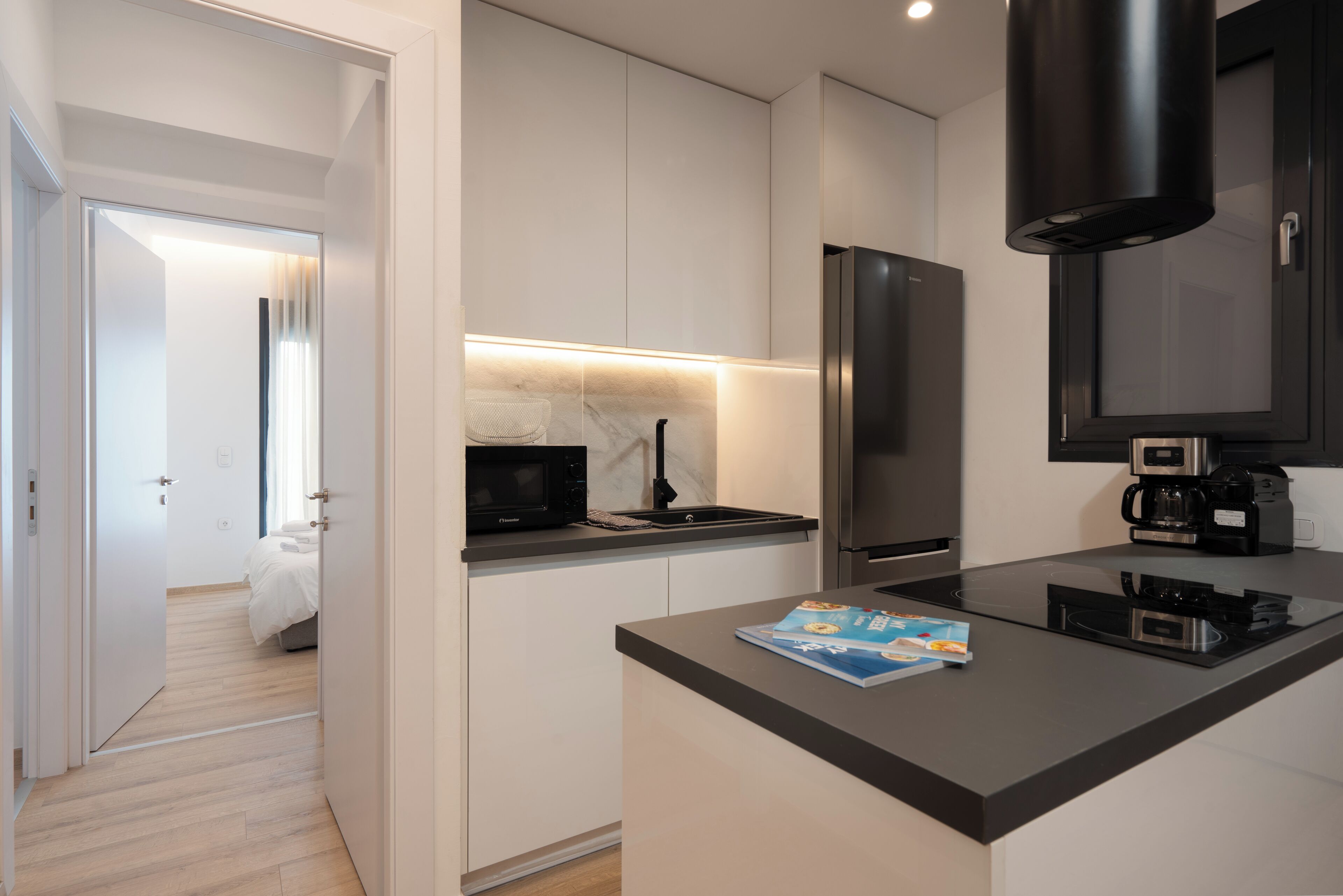 A modern kitchen with white cabinets, a black countertop, a microwave, a coffee maker, and a book on the counter.