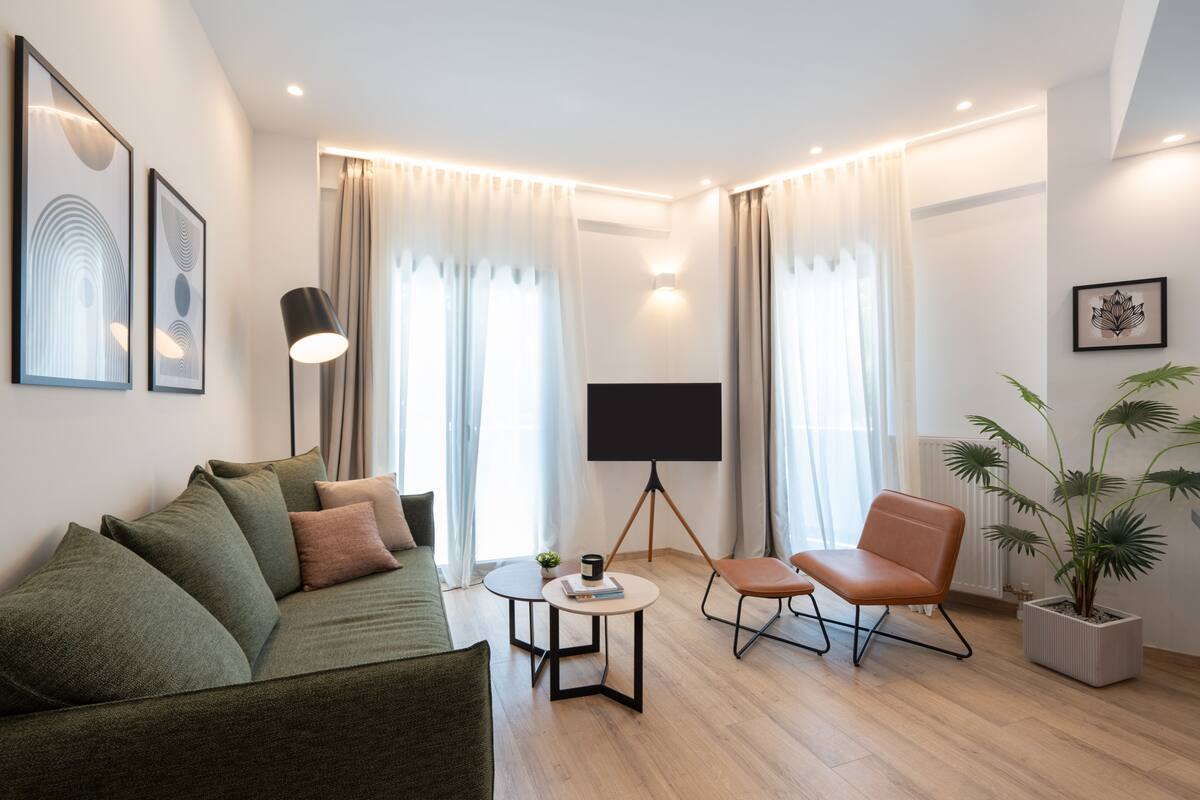 Un salon moderne avec un canapé, une table basse, un téléviseur posé sur un trépied, un fauteuil et une plante en pot.