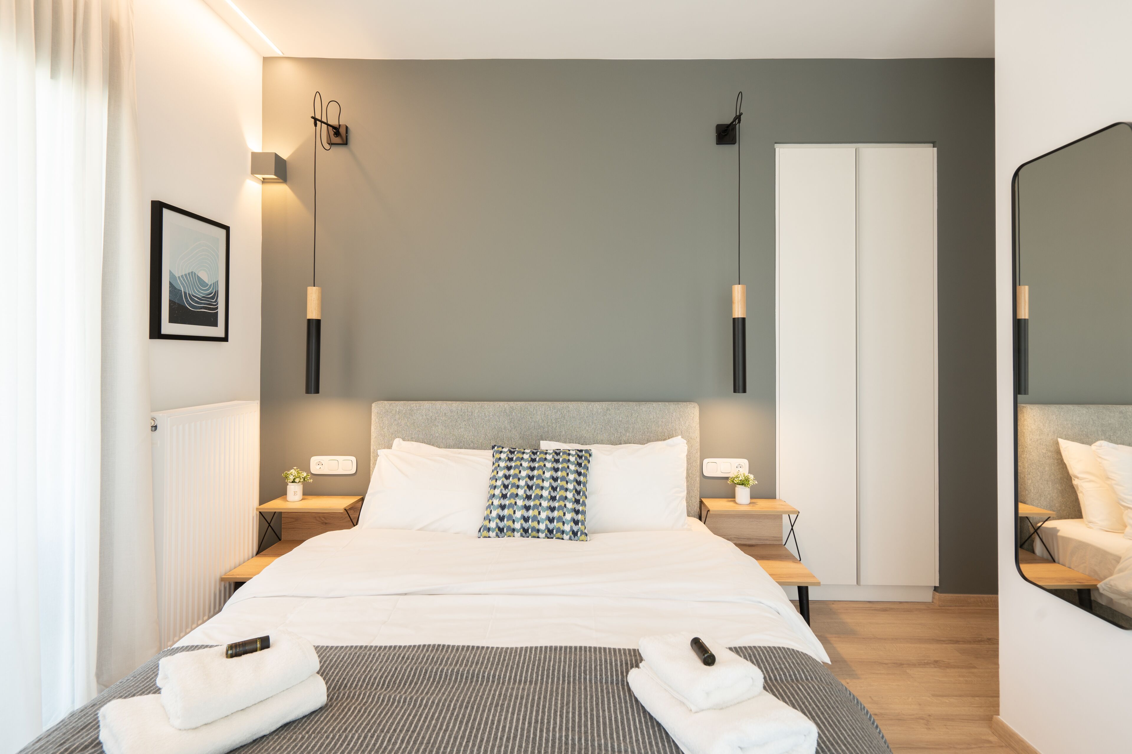 Een moderne hotelkamer met een groot bed, nachtkastjes, een spiegel en een kledingkast.