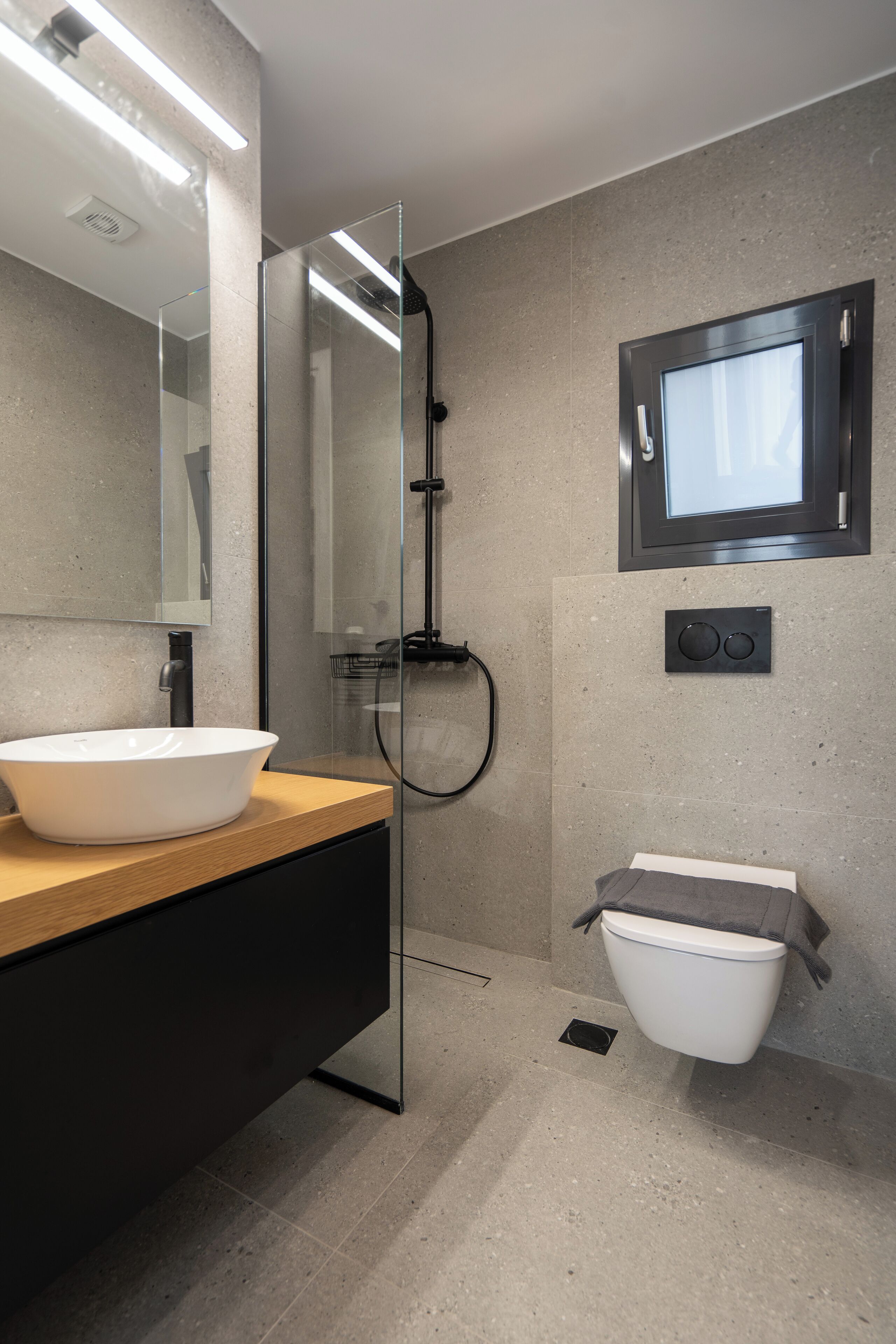 A modern bathroom with a glass-enclosed shower, a large mirror, a wooden vanity, and a white sink.