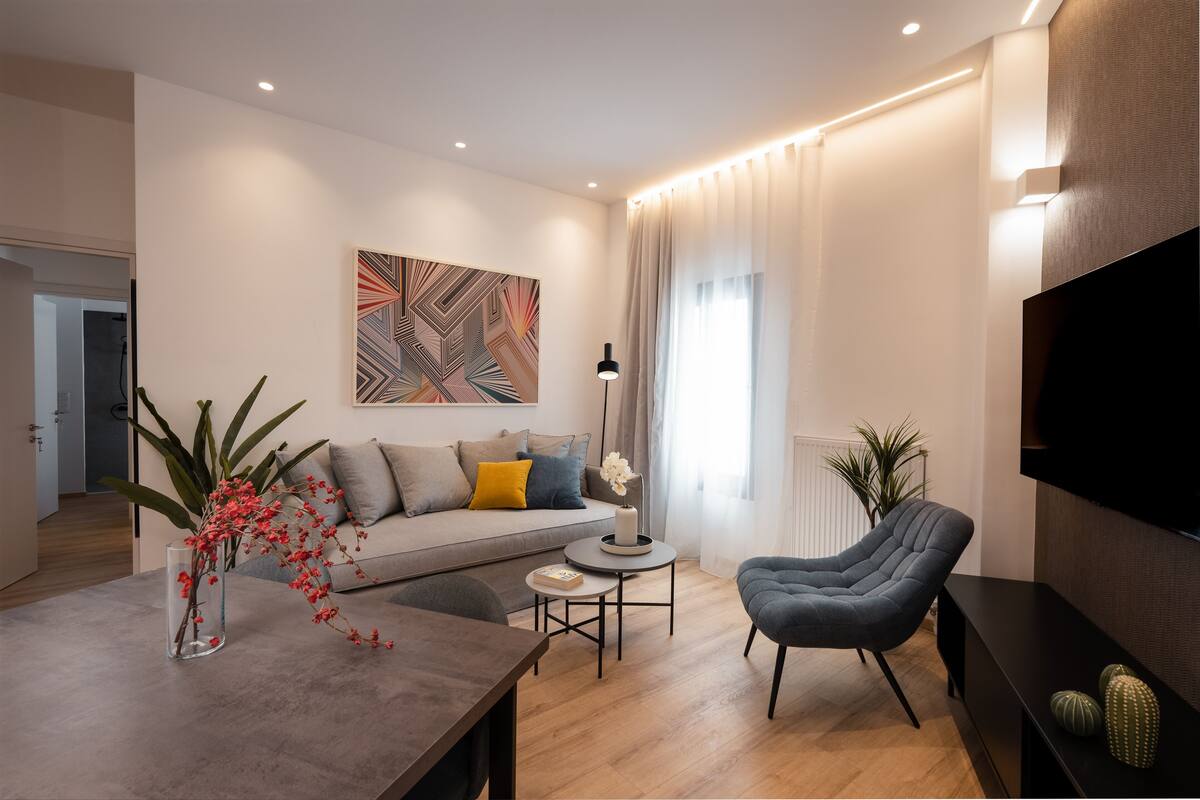 Un salon moderne avec un canapé, une table basse, un téléviseur et un fauteuil.