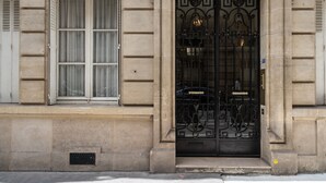 Une façade d’immeuble ornée d’un grand portail en métal noir et d’une fenêtre avec des volets blancs.