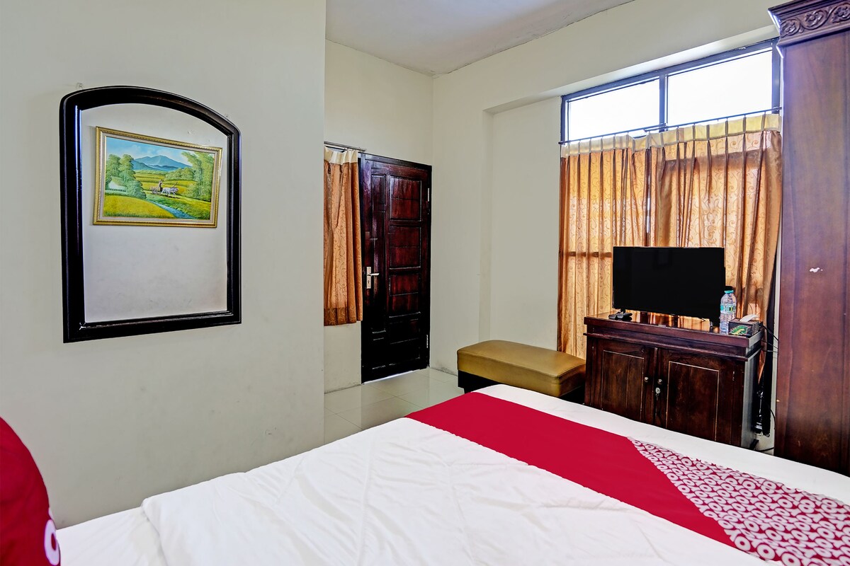 A bedroom with a bed, a television, a wooden cabinet, a framed picture on the wall, and a window with curtains.