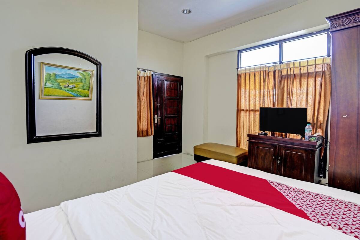 A hotel room with a bed, a TV, a wooden cabinet, a bench, and a painting on the wall.