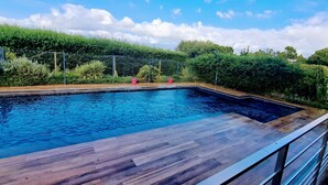 Une piscine rectangulaire dotée d’une terrasse en bois, entourée d’une clôture en métal et d’une végétation luxuriante.