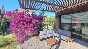 Une terrasse extérieure moderne avec une plateforme en bois, un canapé gris et une table.