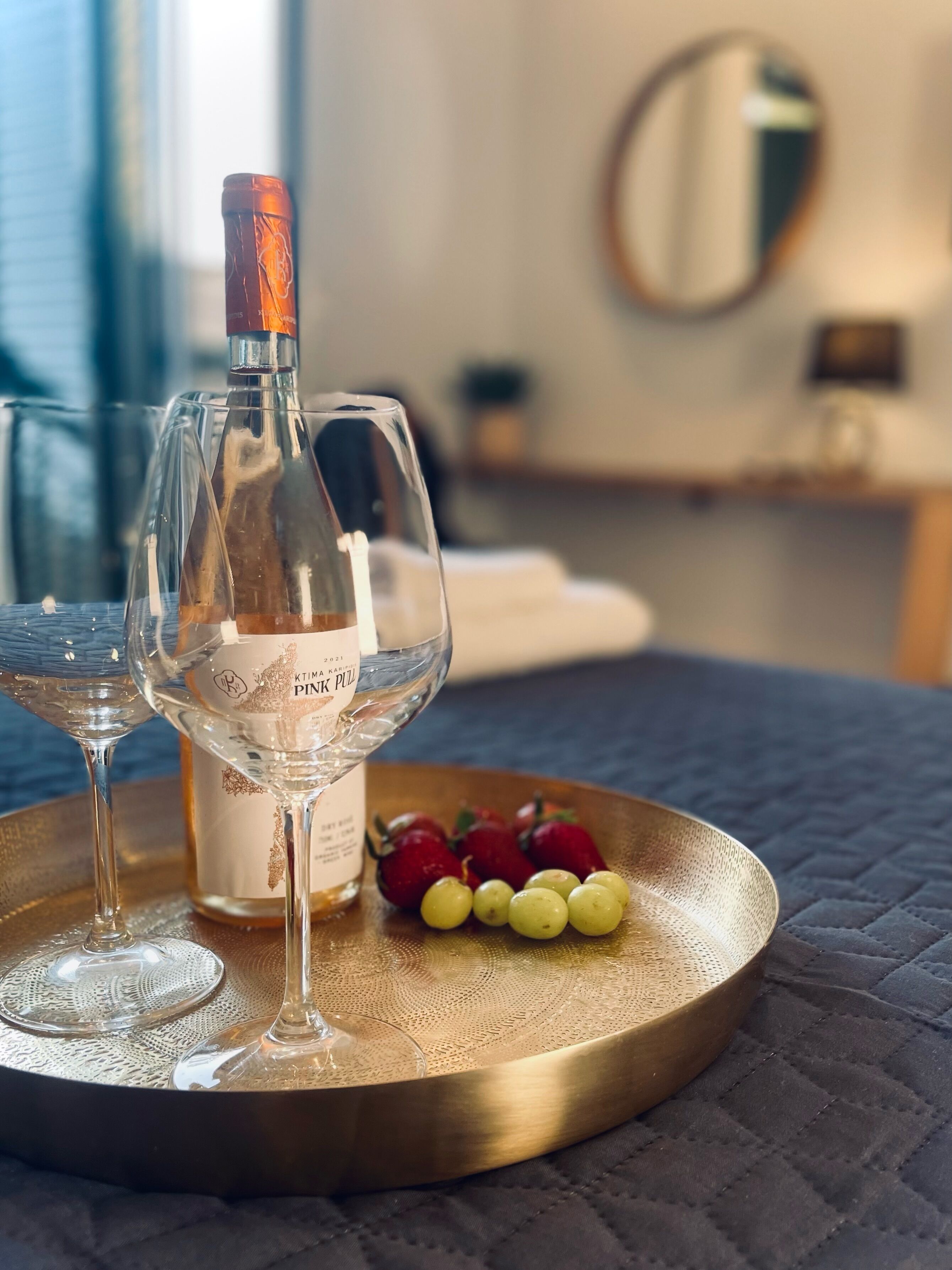Une bouteille de vin rosé, deux verres et une assiette de raisins, le tout sur un plateau.