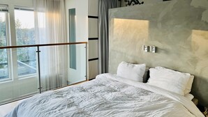 Un dormitorio moderno con una cama grande, un ventanal que da a un balcón y una pared con textura.