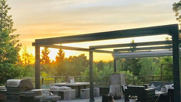 Un patio exterior con una pérgola, mobiliario para sentarse y una parrilla.
