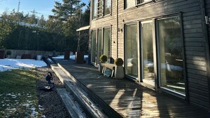 Una casa moderna de dos pisos con grandes ventanales y una terraza de madera.