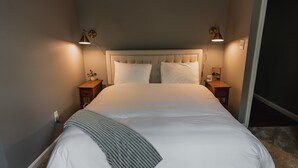 A neatly made bed with a white comforter and pillows, flanked by two bedside tables with lamps, in a room with a simple, clean design.