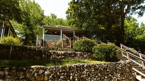 A stone retaining wall with a wooden staircase leading to a house with a porch.