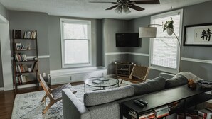 A living room with a sectional sofa, a coffee table, a bookshelf, and a television mounted on the wall.