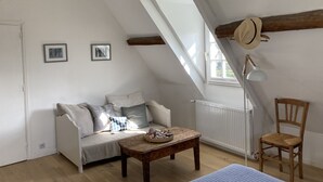 A cozy attic room with a sloped ceiling, a wooden table, a chair, a sofa, and two framed pictures on the wall. - Le Vieux Logis, an idyllic setting (Varengeville-sur-Mer)