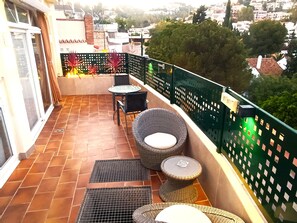 Un balcon doté d’un sol carrelé, de deux fauteuils en osier, d’une petite table ronde et d’une rambarde en métal vert.
