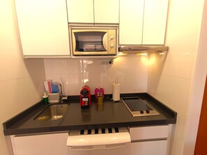 A compact kitchen with a microwave, a kettle, and a kettle holder on the countertop.