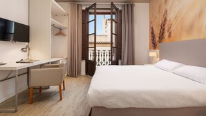 Une chambre d’hôtel avec un lit, un bureau et une chaise, une télévision et une fenêtre avec des rideaux.