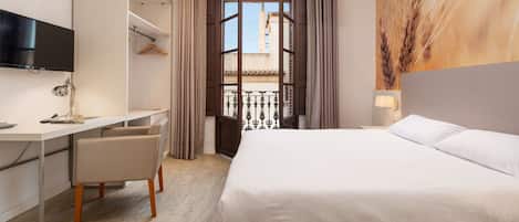 A hotel room with a bed, a desk with a chair, a TV, and a window with curtains.
