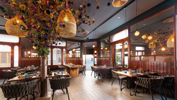 L’intérieur d’un restaurant avec des tables et des chaises en bois, des décorations florales suspendues et des luminaires pendants.