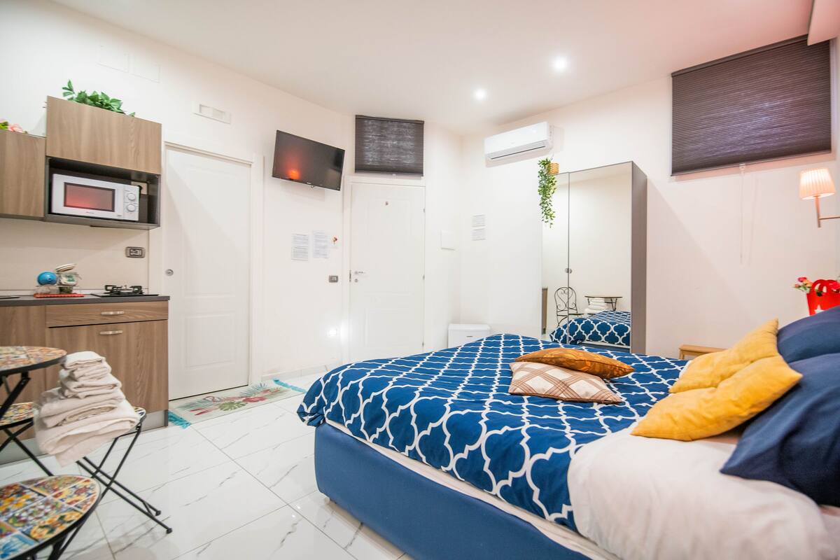 A bedroom with a bed, a TV, a microwave, and a small kitchenette.