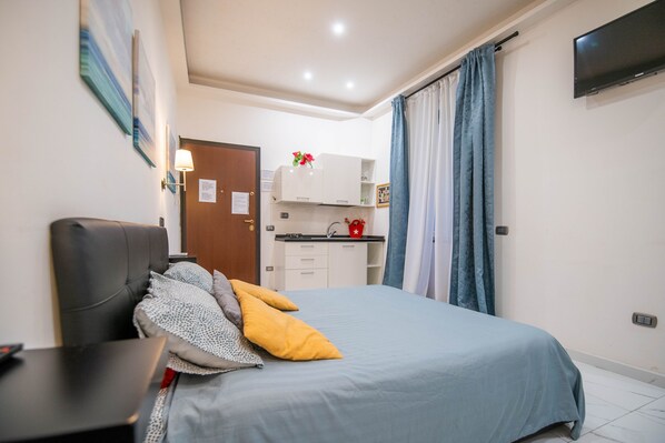 Une chambre comprenant un lit, une table de chevet, un bureau, une armoire, un coin cuisine et un téléviseur.