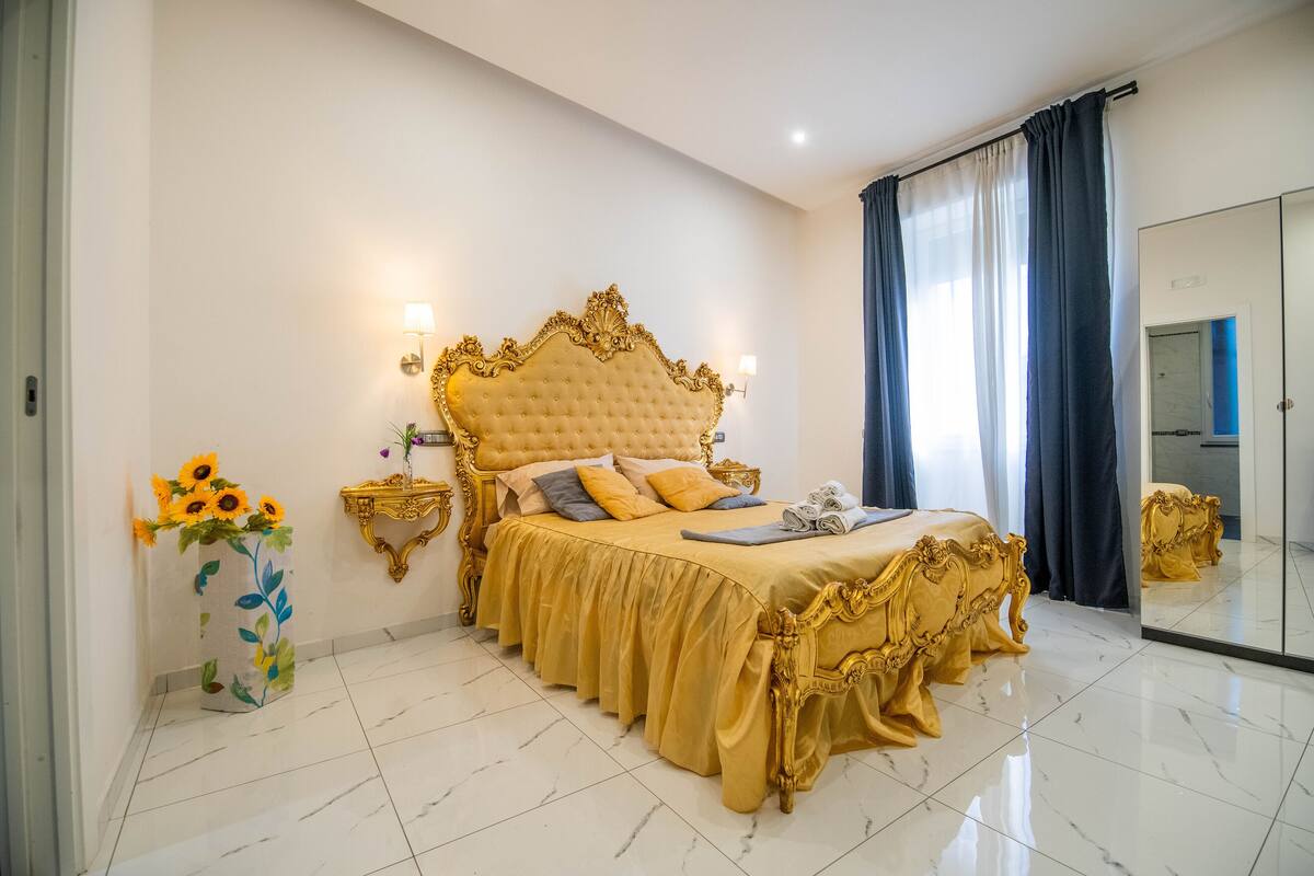 A luxurious bedroom with a large bed, a nightstand, a vase of sunflowers, and a mirror.