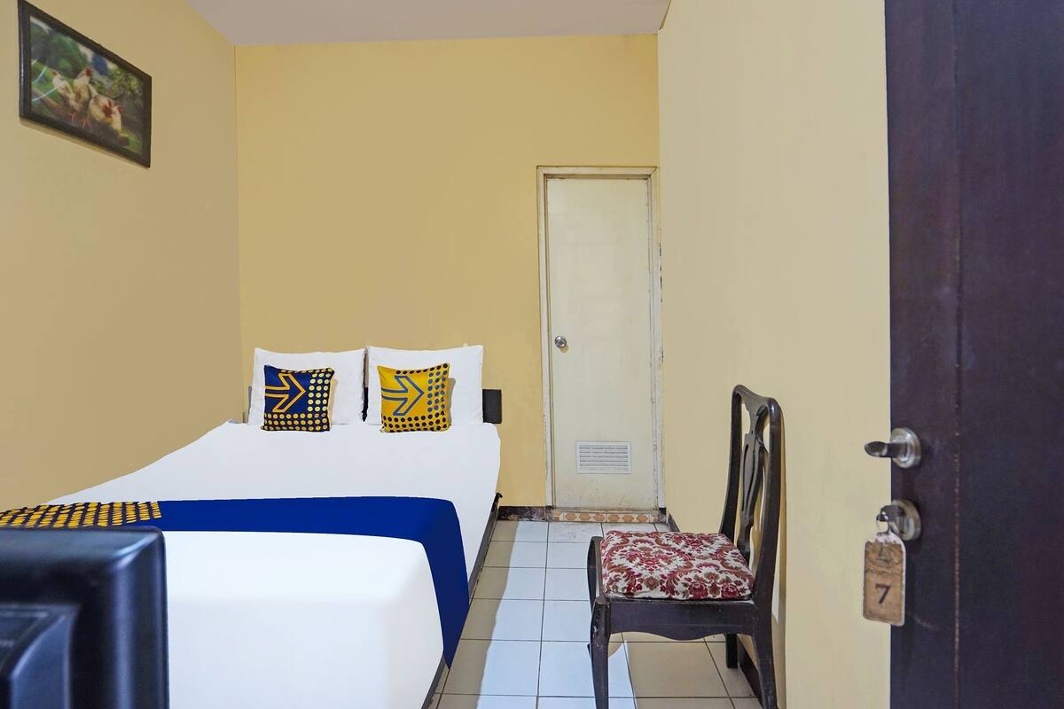 A room with a bed, a chair, a door, and a wall-mounted picture.