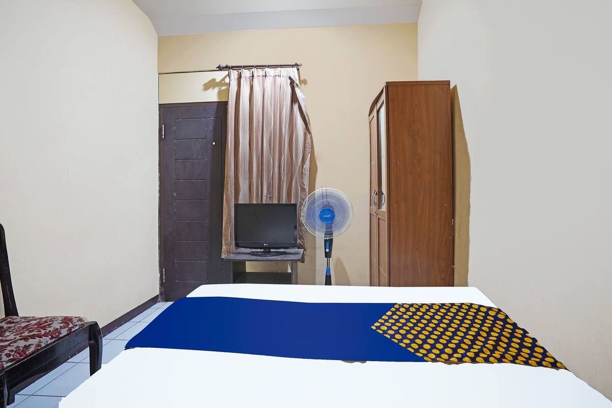 A bedroom with a bed, a television on a stand, a fan, and a wardrobe.