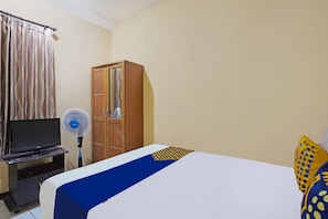 Habitación de hotel con cama, televisor sobre un mueble, armario de madera y ventilador de pie.