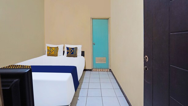 A small, neatly arranged hotel room with a bed, a desk, and a door. - OYO 91695 Hotel Benteng Portugis (Sidoarjo)