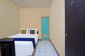 A small, neatly arranged hotel room with a bed, a desk, and a door. - OYO 91695 Hotel Benteng Portugis (Sidoarjo)