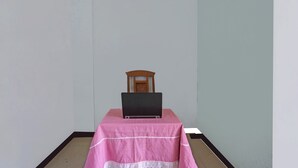 A room with a laptop on a table covered with a pink tablecloth, a wooden chair, and a light-colored wall. - OYO 91695 Hotel Benteng Portugis (Sidoarjo)