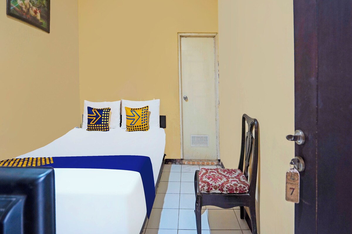 A hotel room with a bed, two pillows, a chair, a door, and a wall with a picture.