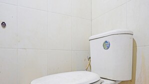 A toilet in a bathroom with white tiled walls and a patterned tile floor. - OYO 91695 Hotel Benteng Portugis (Sidoarjo)