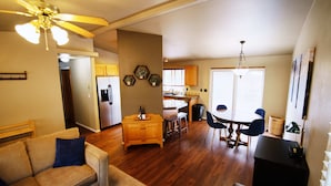 Ein geräumiges Wohnzimmer mit einer Couch, einem Essbereich mit Tisch und Stühlen, einer Küche mit Holzschränken und einem Deckenventilator.