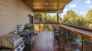 Eine überdachte Terrasse im Freien mit Grill, Barhocker und Blick auf Bäume.