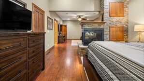 Ein Schlafzimmer mit einem großen Bett, einem Holzkasten, einem Fernseher, einem Steinkamin und einem Deckenventilator.